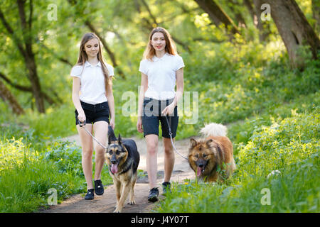 Deux smiling teenage girls walking avec ses chiens dans la région de Spring Park. Concept d'amitié historique Banque D'Images