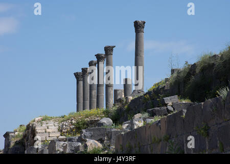 Colonnes du temple de cannelés anciennes ruines à Umm Qais près d'Irbid, Jordanie. Un mur de roche de basalte couvertes de végétation en premier plan et le ciel bleu au-dessus Banque D'Images