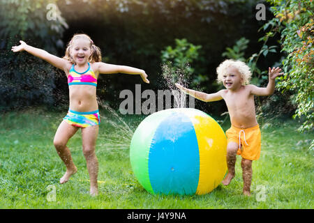 Enfant jouant avec balle jouet jardin arroseur. Courir et sauter pour enfants d'âge préscolaire. Piscine d'été de plaisir de l'eau dans la cour. Les enfants jouent avec tuyau Banque D'Images