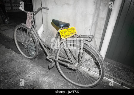 Dirty old pushbike leaning against wall en arrière scène de rue avec un panneau jaune ne pas dépasser véhicule tournant Banque D'Images