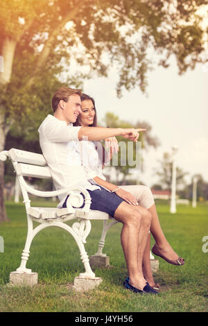 Couple assis sur un banc de parc, pointant l'homme en face d'eux Banque D'Images