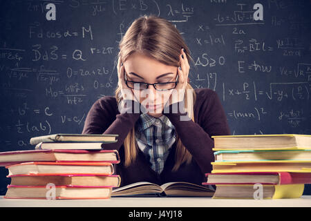 Jeune étudiant à l'expression désespérée assis à un bureau et en regardant ses livres Banque D'Images