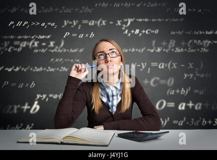 Jeune étudiant à l'air pensif assis à un bureau avec des formules mathématiques sur sa tête Banque D'Images