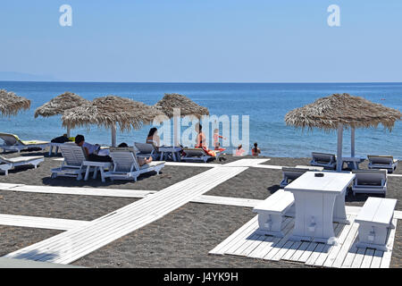 Sur un lit de repos touristiques sous des parasols de paille à Perissa, Santorin, Cyclades, Grèce Banque D'Images