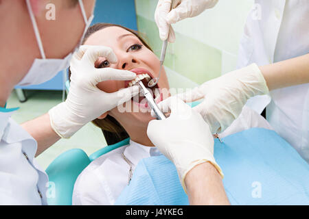 Closeup portrait dentiste, son assistant d'effectuer un examen approfondi de la procédure dentaire, l'extraction dentaire sur les jeunes patients de sexe féminin, couché dans une chaise, Banque D'Images