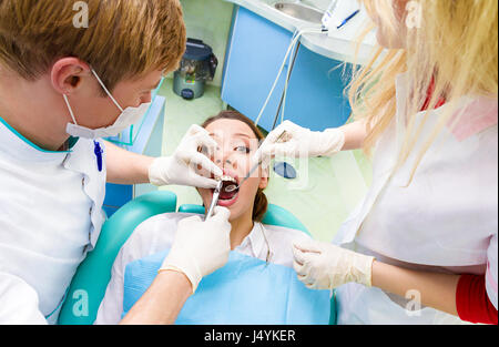 Closeup portrait dentiste, son assistant d'effectuer un examen approfondi de la procédure dentaire, l'extraction dentaire sur les jeunes patients de sexe féminin, couché dans une chaise, Banque D'Images