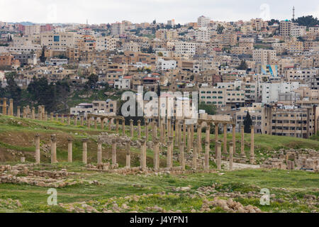 Colonnes et chapiteaux en pierre de la rue à colonnade dans l'ancienne cité romaine de Jerash, ville de commerce Jordanie. La ville moderne s'est vu dans l'arrière-plan. Banque D'Images