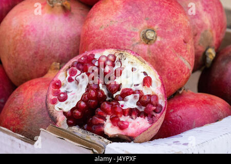 Super fruit rouge juteux des grenades dans une boîte au marché plein air avec un fruit coupé en deux pour montrer le livre blanc tissu spongieux et les arilles. Banque D'Images