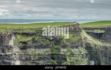 Les gens qui marchent sur un chemin au sommet des falaises de Moher sur un ciel couvert, nuageux et sombre jour, Irlande Banque D'Images