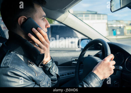 Jeune homme en utilisant son téléphone en conduisant la voiture. La conduite dangereuse Banque D'Images