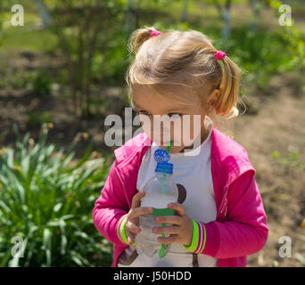 Petite fille mignonne l'eau potable de la bouteille en plastique. photo ensoleillée Banque D'Images