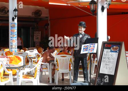 Les touristes se détendre à la terrasse d'un café avec une statue de Stan Laurel tenant un menu, Torremolinos, Malaga Province, Andalusia, Spain, Europe de l'Ouest. Banque D'Images