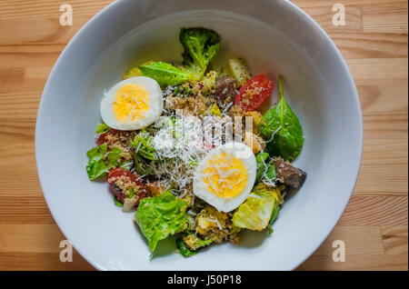 Une salade verte dans un bol blanc sur une table en bois, avec un œuf dur Banque D'Images