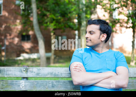 Stock Photo - Closeup portrait souriant, heureux, jeune homme ordinaire en chemise bleue assis sur le banc en bois, détendue à côté d'isolent, tr Banque D'Images