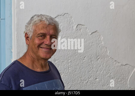 L'île d'Amorgos, Grèce - Octobre 2015 : Portrait of a Smiling man, in front of white rendus mur dans Katapola, Grèce Banque D'Images