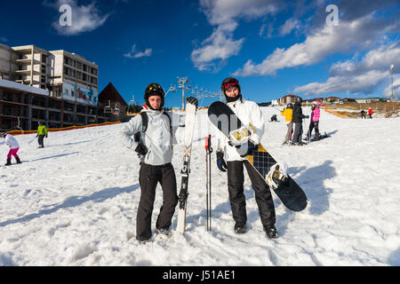 Heureux les jeunes hommes en combinaisons de ski, casques et lunettes de ski skis et snowboards avec permanent dans une station de ski en hiver Banque D'Images