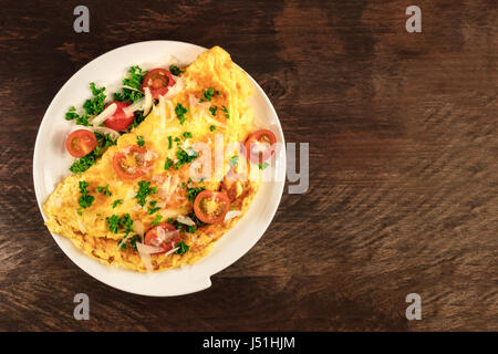 Une photo d'une omelette aux tomates cerises, le persil et le fromage râpé, tourné à partir de ci-dessus sur une texture rustique en bois avec une place pour le texte Banque D'Images