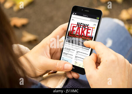 La technologie des médias et concept de vie moderne : young woman with smartphone lecture fake news au parc Banque D'Images