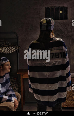 Prisonnière portant des uniformes de prison debout avec son retour près d'un autre prisonnier assis sur un lit dans une cellule de prison Banque D'Images