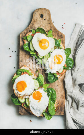 Petit-déjeuner sain des sandwichs. Toasts de pain frit avec des oeufs et des légumes sur planche de bois sur fond de marbre gris, vue du dessus. L'alimentation, l'h Banque D'Images