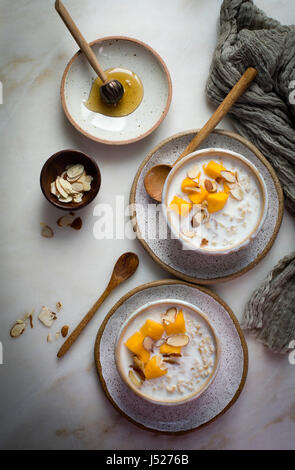 Petit déjeuner porridge d'avoine au lait garnis de mangues hachées et les amandes dans un bol en céramique sur une table en marbre sur une vue supérieure Banque D'Images