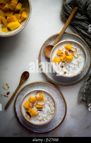 Petit déjeuner porridge d'avoine au lait garnis de mangues hachées et les amandes dans un bol en céramique sur une table en marbre sur une vue supérieure Banque D'Images