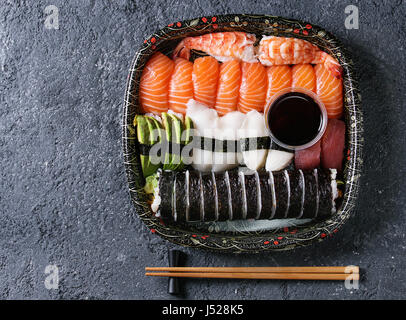 Set à Sushi nigiri et rouleaux de sushi en boîte de livraison de nourriture en plastique avec de la sauce soja et baguettes sur pierre noire texture background. Vue de dessus avec l'espace. Banque D'Images
