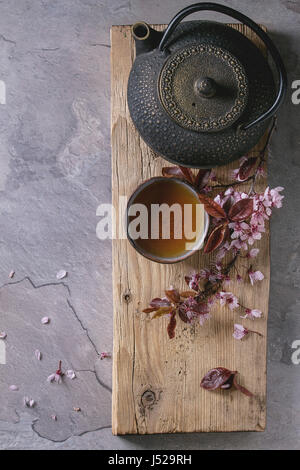 Fer noir, théière et tasse de thé en céramique traditionnel en bois servant de carte avec des fleurs rose blossom cherry branch sur fond texture gris. Haut Banque D'Images