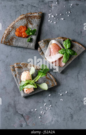 Crêpes crêpes noir avec variété de remplissage de sel caviar rouge, jambon, saumon pate de poisson, salade verte sur fond gris metal texture. Vue d'en haut Banque D'Images