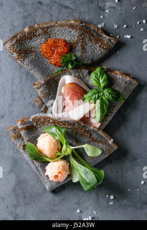 Crêpes crêpes noir avec variété de remplissage de sel caviar rouge, jambon, saumon pate de poisson, salade verte sur fond gris metal texture. Vue d'en haut Banque D'Images