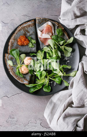 Crêpes crêpes noir avec variété de remplissage de sel caviar rouge, jambon, saumon pate de poisson, salade verte avec plus de serviettes linge textile texture gris backgrou Banque D'Images