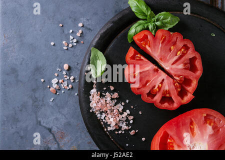 Ensemble et les tranches de tomates Coeur de boeuf bio. Tomate coeur de boeuf avec du sel rose et basilic sur planche en bois noir sur gris bleu metal textur Banque D'Images