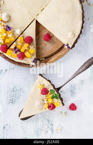 Des tranches de tarte au chocolat décoré par la mangue, framboises, menthe, riz soufflé et fleurs comestibles avec morceau de gâteau sur une pelle à tarte sur texte blanc Banque D'Images