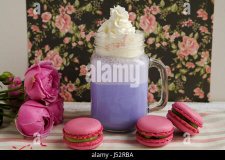 Café pourpre en pot Mason Tasse stylisée avec ses macarons et les roses et une décoration colorée sur fond de motif floral. Lait frappé aux bleuets. Licorne Banque D'Images