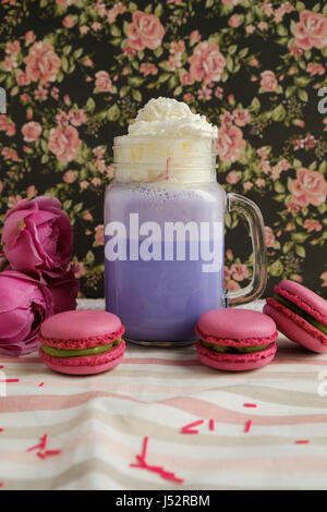 Café pourpre en pot Mason Tasse stylisée avec ses macarons et les roses et une décoration colorée sur fond de motif floral. Lait frappé aux bleuets. Licorne Banque D'Images