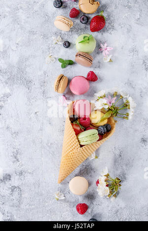 Variété de desserts sucrés macarons français colorés avec différents fourrages servis en cornet gaufré à la menthe et les baies fraîches plus de texture gris backgrou Banque D'Images