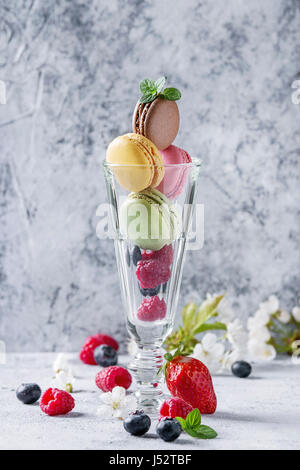 Variété de desserts sucrés macarons français colorés avec différents fourrages servis en verre avec fleurs de printemps et de baies fraîches plus de texture gris retour Banque D'Images