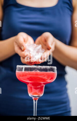 Une femme avec un tee-shirt bleu verser les glaçons dans ses mains en watermelon marguerite photographié à partir de la vue de face. Banque D'Images