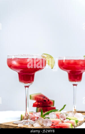 Watermelon marguerite dans verres debout sur une planche en bois photographié à partir de la vue de face. Des cubes de glace, de la pastèque en tranches, tranches de lime et de menthe Banque D'Images