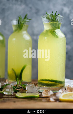 Limonade parfumée à la menthe et romarin servi dans une bouteille photographié sur une planche en bois avec un fond gris à partir de la vue de face. Les tranches de citron, lime Banque D'Images