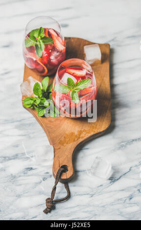 Orange sanguine et Sangria estivale de fraises. Des cocktails de fruits vin rose rafraîchissante dans les verres avec de la glace et la menthe sur planche de bois sur le marbre gris background Banque D'Images