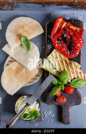 Ingrédients pour faire des sandwichs de pain pita. Les légumes grillés, le basilic et le fromage feta avec le pain plat sur sol en bois servant au retour de texture gris Banque D'Images