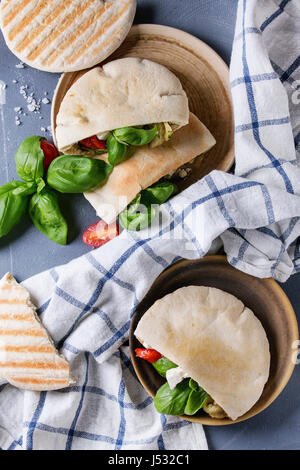 Sandwichs de pain pita avec légumes grillés paprika, aubergine, tomate, basilic et feta fromage servi sur la plaque en terre cuite sur fond noir en gris. Banque D'Images