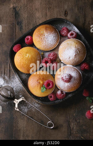 Muffin citron maison cupcakes avec les framboises, le sucre en poudre, menthe, servi dans la plaque de bois carré avec tamis plus vieux vintage background en bois foncé Banque D'Images