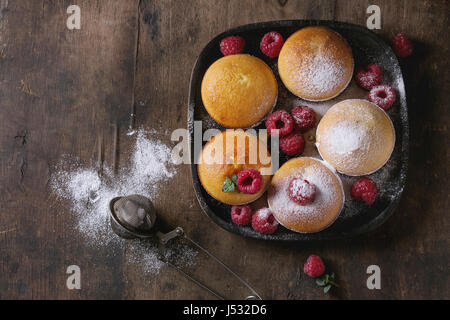 Muffin citron maison cupcakes avec les framboises, le sucre en poudre, menthe, servi dans la plaque de bois carré avec tamis plus vieux vintage background en bois foncé Banque D'Images