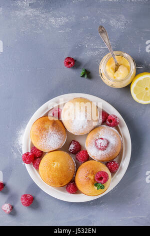 Muffin citron maison cupcakes avec les framboises, le sucre en poudre, menthe, servi avec un pot de lait caillé de citron et citrons sur gris bleu stone texture backg Banque D'Images