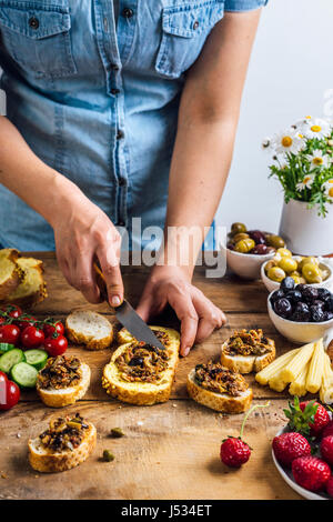Une femme la diffusion de tapenade d'olives sur une tranche de pain de maïs photographié à partir de la vue de face. Trois types d'olives marinées, baby corns, fraises, ville énorme Banque D'Images