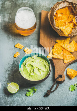 Croustilles de maïs mexicain, sauce guacamole frais et un verre de bière sur sol en bois servant de sélection sur table béton gris background, selective focus, vertical com Banque D'Images