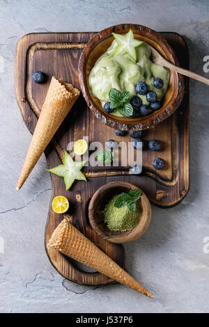 Bol de thé vert matcha glace élastique souple avec les feuilles de menthe, la carambole, la chaux, les bleuets et les cônes alvéolés en bois sur bois avec du conseil spoo Banque D'Images