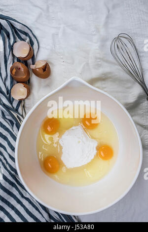 Les oeufs et le sucre dans un bol prêt à être emmené photographié en vue de dessus. Un fouet et coquilles d'œufs sont sur le côté. Banque D'Images